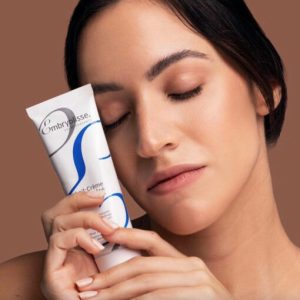 A woman holding a tube of Lait Crème Concentré next to her face