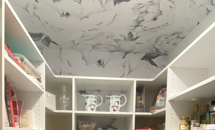 Ceiling, wall and some shelves covered with the black and white wallpaper of peonies.